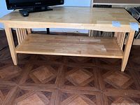 Full view of light wood rectangular coffee table with lower shelf under the tabletop and tapered legs.