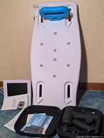 White portable shower bench with blue cushioned headrest on carpet against wallpapered wall, no visible brand markings, condition appears good but untested.