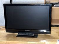Front view of a black Dynex flat screen TV measuring 21 inches on a stand, with a remote placed in front.