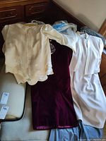 Photo showing three formal women's clothing items: a white blazer with floral embroidery and a dark burgundy velvet skirt, a cream colored dress, and a pale pink dress with matching jacket.