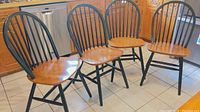 Four Windsor style wooden chairs with green painted backs and legs and natural wood seats, arranged on kitchen tile floor.