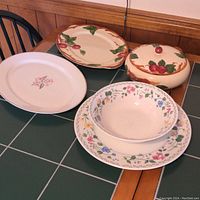 View of all five pieces including Franciscan Apple platter, covered bowl, Syracuse Patricia platter and bowl, and Farberware platter and bowl, arranged on a tiled table.