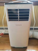 Front view of white Frigidaire portable air conditioner with vents and power cord visible.
