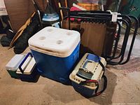 Photo showing gravity chair frame, large Igloo cooler, two medium coolers, and pet carrier in basement setting.