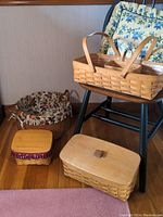 View of five Longaberger baskets and a floral Longaberger pillow displayed near a black wooden chair with a floral cushion.