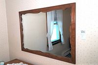 Close view of the wooden framed wall mirror mounted on the wall with a window reflected.