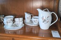 Full vintage Noritake Rossina luncheon set arranged on wooden cabinet, including coffee pot, cream pitcher, sugar bowl, four plates, five cups all with floral rose pattern and silver trim.