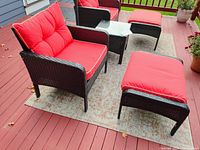 PatioJoy armchair with cushioned seat and back in red, dark woven frame, placed on patio rug with matching ottoman nearby.