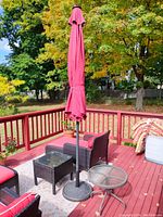 Wide view showing red patio umbrella closed and black woven style side table with red cushions outdoor on the deck.