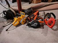 Photo showing lot of power tools including yellow electric orbital car waxer, black and orange Black & Decker circular saw and reciprocating saw, orange Black & Decker hedge trimmer.