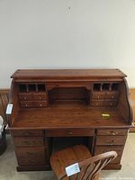 Front view of wooden roll top secretary desk with multiple drawers and compartments, showing interior and workspace.