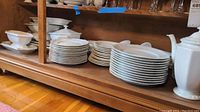 Wide shot of stacked dinner plates, bowls, and teapot on wood shelf showing large portion of service