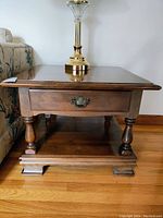 Square wooden coffee table with drawer and lower shelf, shown front view with lamp on top