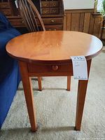 Front view of the oval wood side table with a small drawer visible underneath the tabletop.