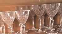 Shelf of faceted crystal wine glasses with smaller set in front and larger behind, showing detailed cut designs.