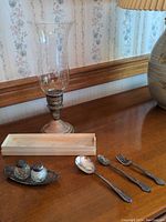 Photo showing sterling silver weighted candle holder with an etched glass hurricane shade, small salt and pepper shakers on a silver tray, two spoons and one fork.