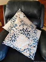Two matching decorative pillows placed on a black chair showing the front floral leaf pattern.