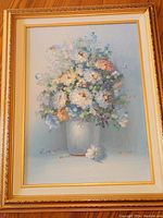 Full view of one framed floral painting, showing a bouquet of flowers in a vase and gold frame.