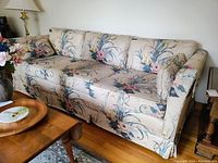 Front angled view of the floral upholstered couch showing one arm and cushions under even indoor lighting.