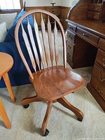 Wooden desk chair showing front and side view, highlighting wood finish, contoured seat, and caster wheels.