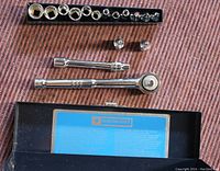 Complete socket set items laid out on fabric background, includes sockets in black tray, ratchets, extension bars, and box.