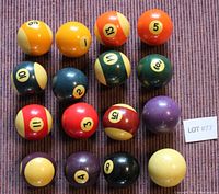 Top-down view of 16 assorted pool balls arranged on a fabric surface, showing wear and color variation.