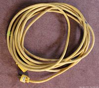 Full view of coiled yellow extension cord on floor, showing length and visible wear.