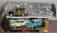 Three 1/24 scale die cast cars in original packaging. Includes black woody, cream 1955 Chevy Bel Air coupe, and turquoise 1955 Chevy Bel Air Nomad station wagon.