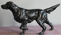 Side view of black cast metal dog figurine showing detailed fur texture and raised front paw.