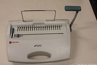 Front view of ACCO Rexel CB255 coil binding machine showing the handle, punch pins and part of the adjustable margin control.