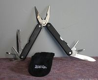 Open view of the multi-tool with all tools extended and the black fabric holder placed below it.