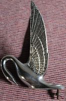 Side view of metal swan hood ornament with detailed engraved wings and mounting bolt visible
