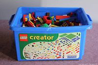 Blue plastic Lego Creator labeled bin filled with assorted Lego blocks of various shapes and colors.
