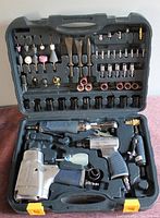 Full view of open hard plastic case showing pneumatic impact gun, die grinder, offset impact tool, air chisel and various accessories including grinding stones, sanding drums, chisels and sockets organized in molded compartments.