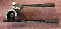 Side view of manual pipe bender showing adjustable protractor scale and leverage handle with textured grip