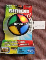 Simon Game in micro series packaging, green, red, yellow, blue quadrant buttons, game lit up red in one photo and yellow in another, unopened packaging