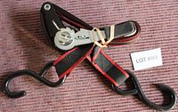 Ratchet tie down strap folded with visible metal ratchet mechanism, coiled black and red strap, and black coated S-hooks for securing cargo