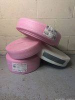 Four rolls of FoamSealR sill plate gasket foam, two stacked pink rolls and one white roll shown, stored against a concrete wall.