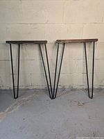 Full view of two hairpin style table legs set against a white wall and concrete floor.