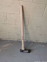 Full view of Collins splitting axe with Hickory handle leaning against a wall on concrete floor