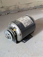 Motor assembled showing side label with specifications, black cylindrical body, and front-mounted pulley wheel with metal housing.