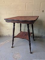 Full side view of the antique parlour table showing the square top, lower shelf, turned legs, and claw feet on casters.