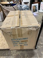 Sealed cardboard box with label showing Style No P9852, Size SIM/LXL, Quantity 60 PCS, box slightly damaged at the corner