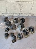 Photo showing 13 caster wheels arranged on concrete floor against a wall including sets of three, and pairs, with varying wheel diameters around 2 to 3 inches.