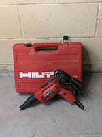 Hilti TS 12 corded drill resting against the red carrying case on concrete floor.