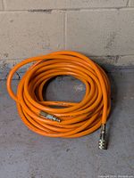 Coiled orange 3/8" air tube hose on concrete floor showing full coil length and bright color.