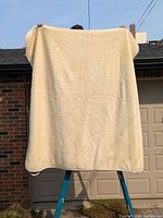 Full view of the king size wool mattress cover held up showing full size and off-white textured fabric.