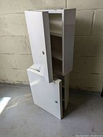 Two white metal locking cabinets stacked with doors partially open, showing interior shelves.