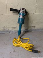 Full front view of the Makita disc grinder standing upright with yellow power cord coiled on the ground.