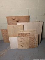 Assortment of plywood pieces stacked against wall showing multiple sizes and wood grain variations